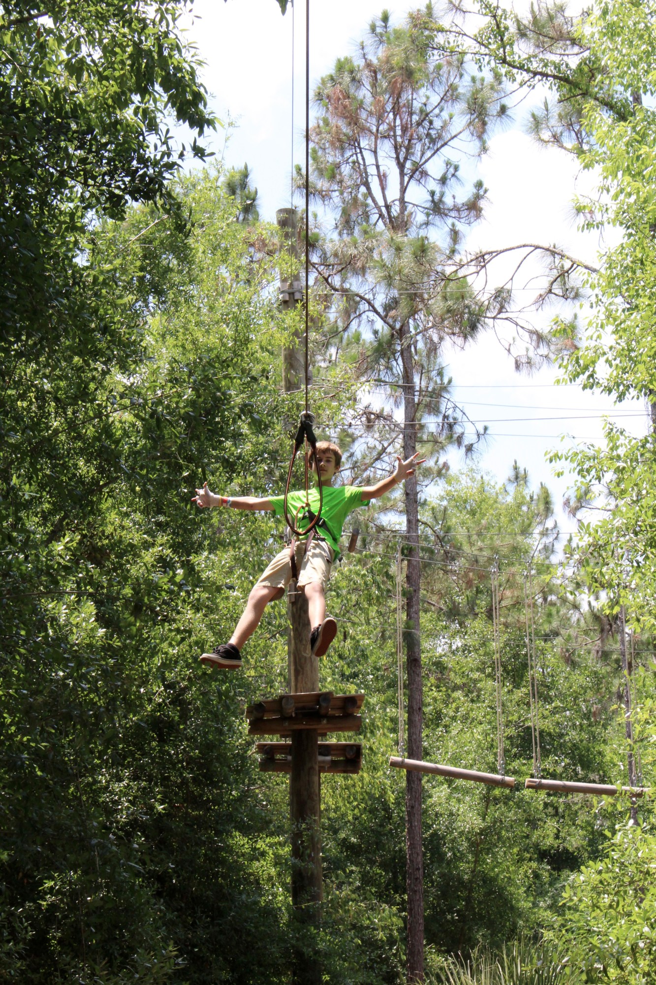 Person in green shirt ziplining through a forested area with arms outstretched.