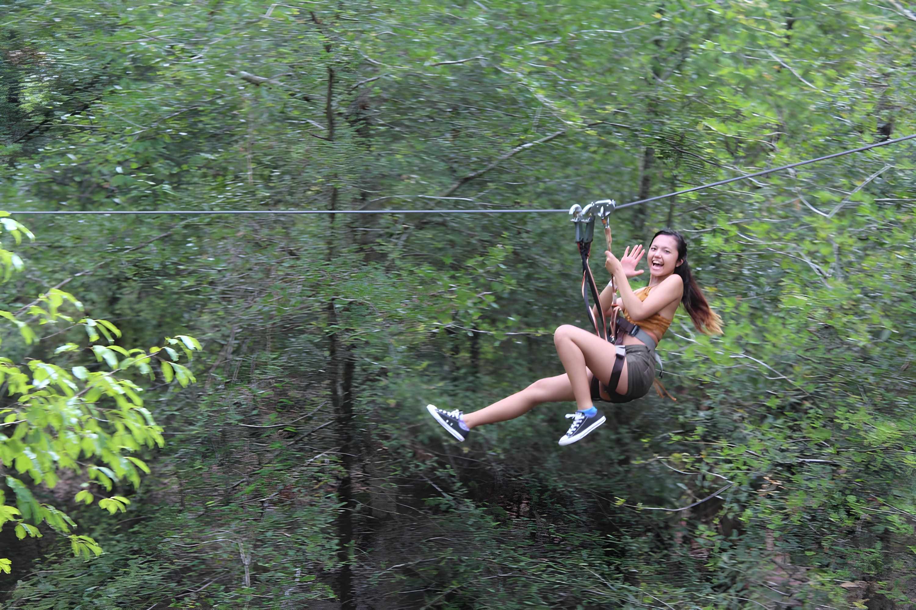 Person ziplining through forest, smiling and waving.
