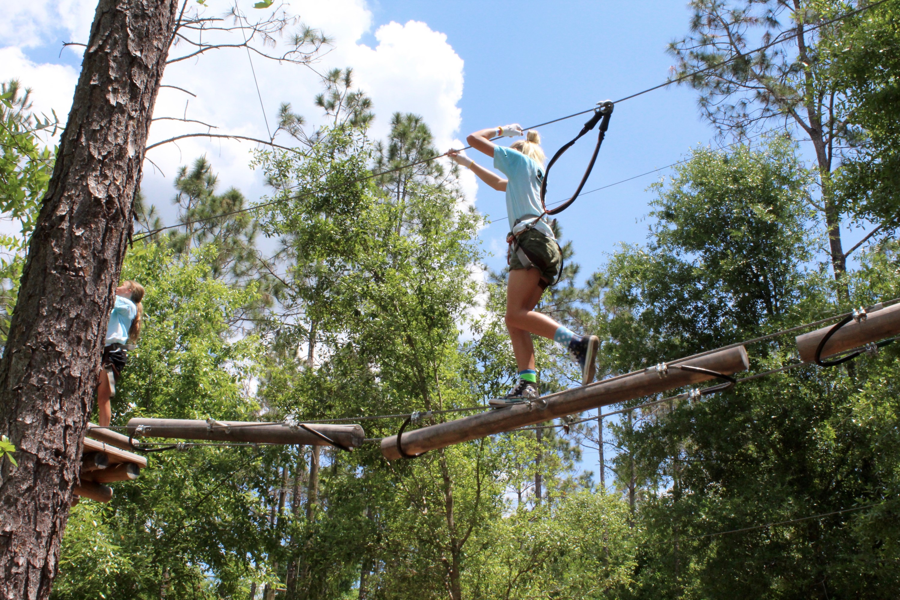 Two people in harnesses balancing on ropes in a treetop adventure course.