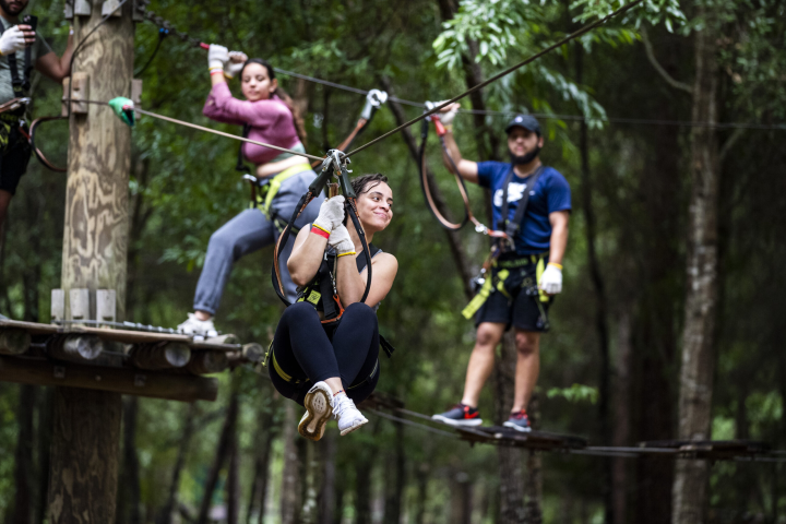 Three people on zip line and ropes course in a forest setting.