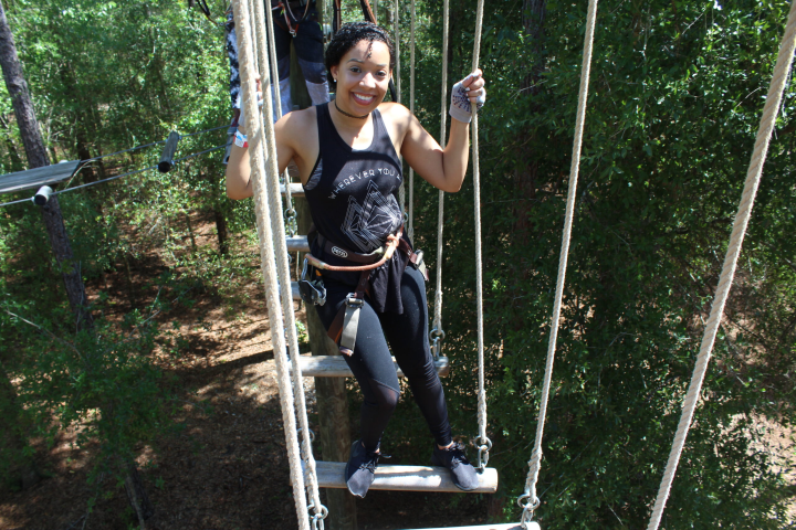 Person smiling while climbing a rope ladder among trees.