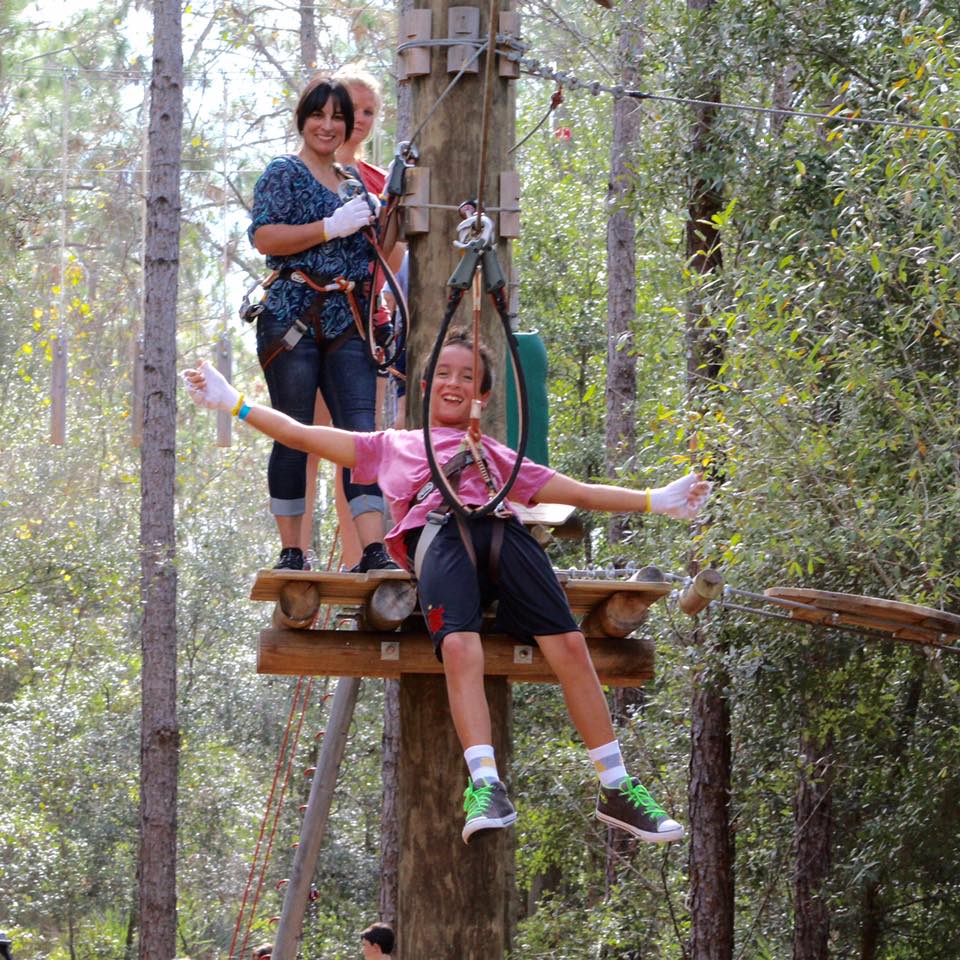 Two people at a zip line platform; one is harnessed, ready to glide.