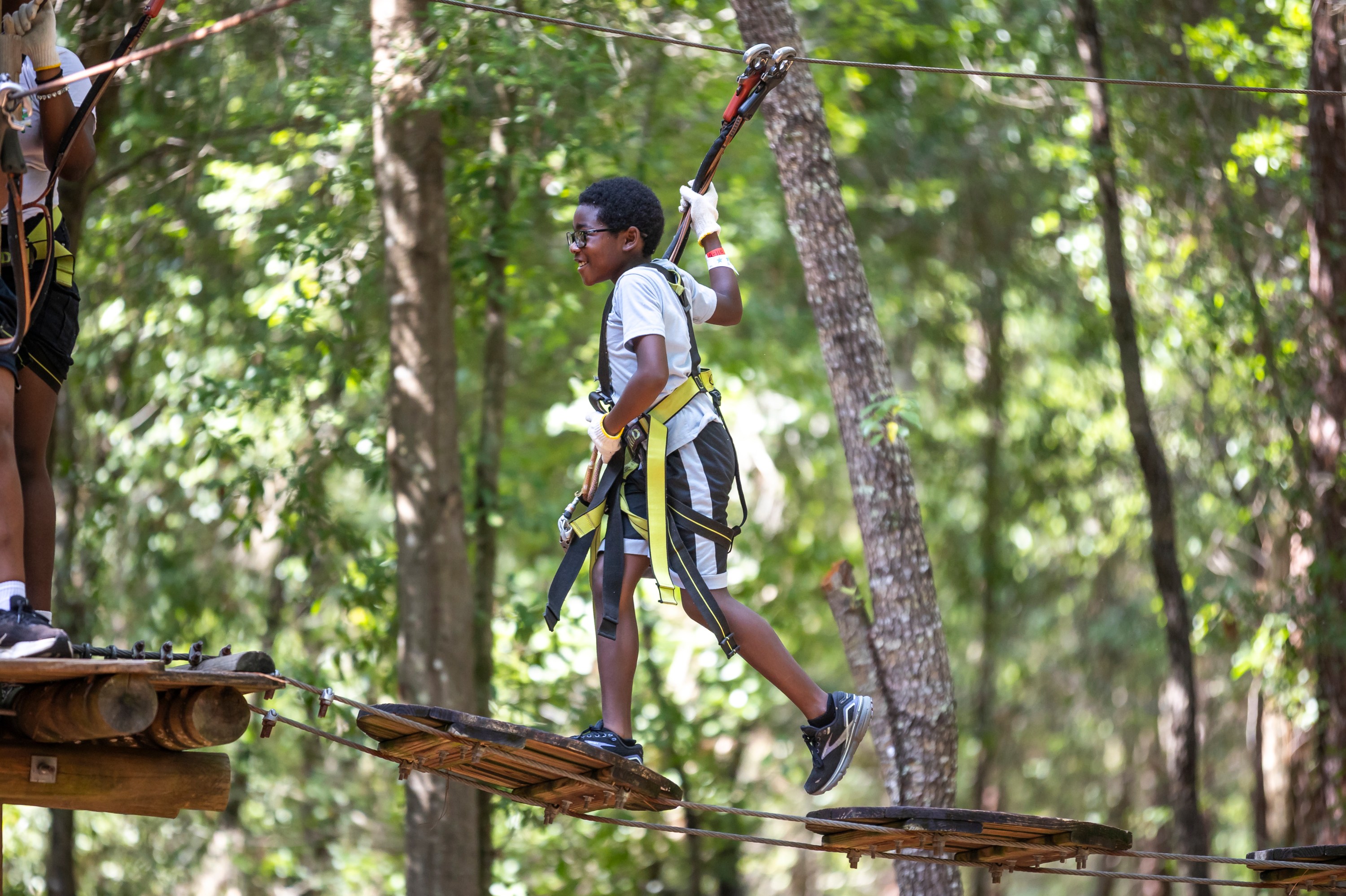 Child crossing a rope bridge in a harness in a forest adventure park.
